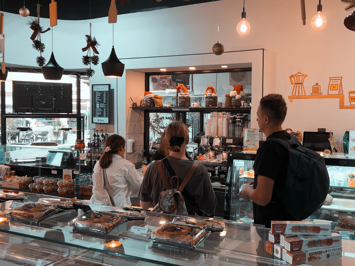 Inside StoArtos Coffee Bakery: customers at the counter with pastries, coffee bar and warm pendant lighting